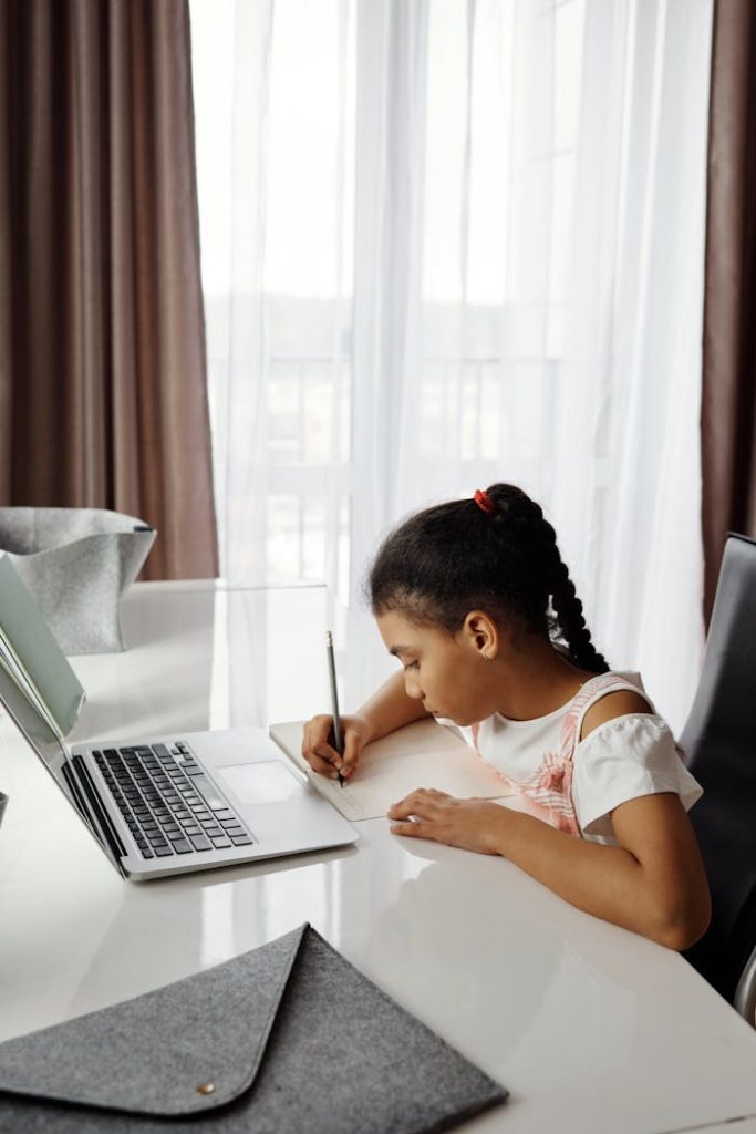 A young girl focuses on her studies at home using a laptop, emphasizing online learning.