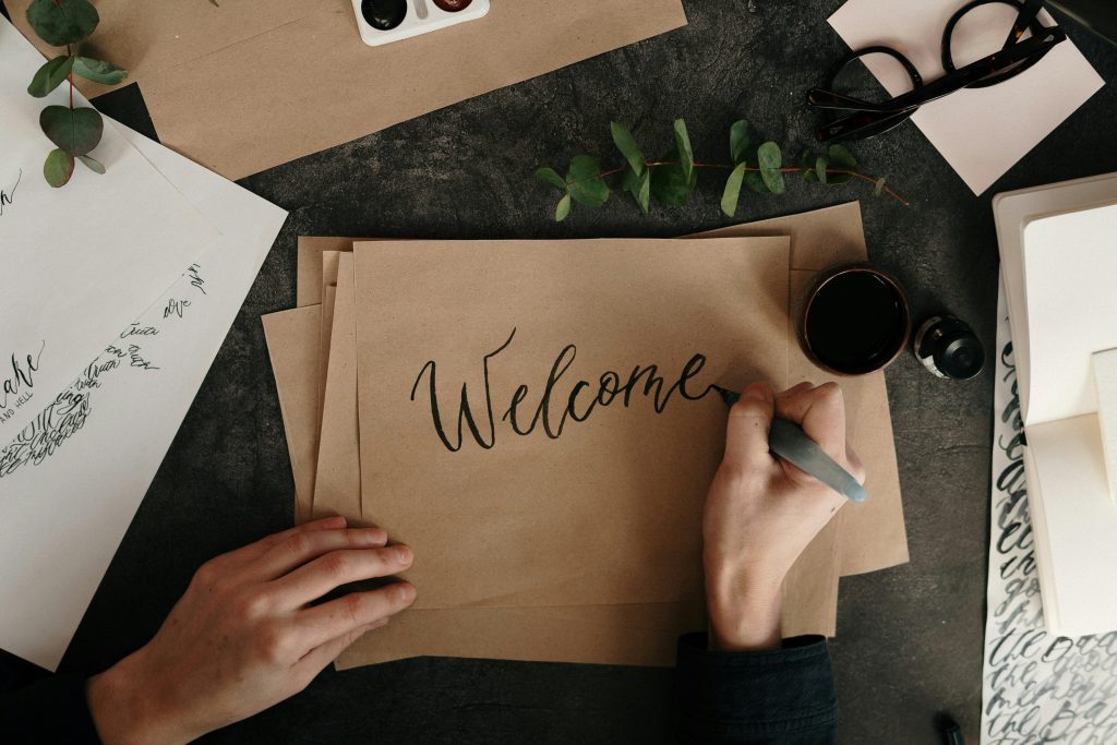 Handwriting a welcome card with calligraphy on craft paper, surrounded by art supplies.