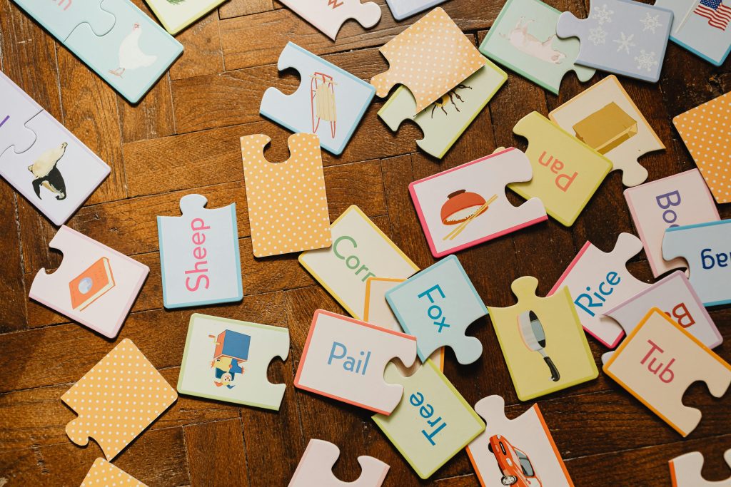 A scattered collection of educational puzzle pieces showcasing words and images on a wooden floor.